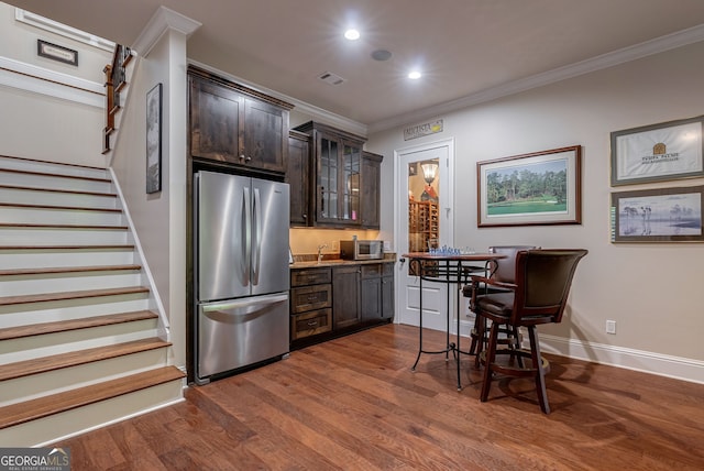 kitchen with dark wood-style flooring, ornamental molding, freestanding refrigerator, glass insert cabinets, and dark brown cabinetry