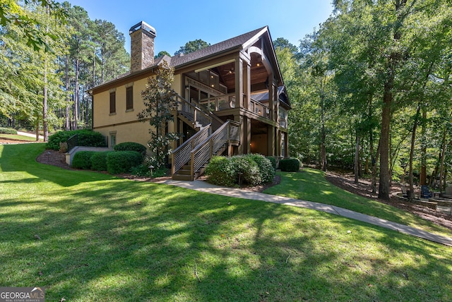 back of house with stucco siding, a yard, a chimney, and stairs