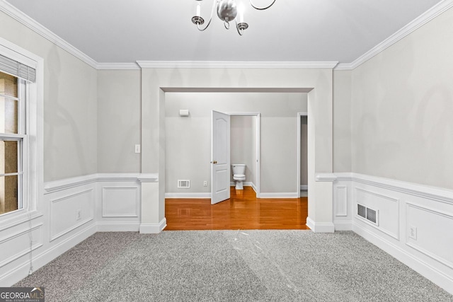 carpeted spare room with a wainscoted wall, visible vents, crown molding, and a decorative wall