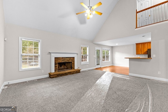 unfurnished living room with high vaulted ceiling, baseboards, carpet flooring, and a stone fireplace