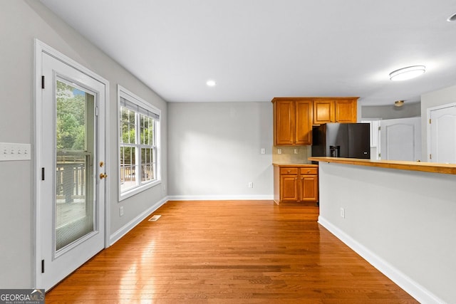 kitchen featuring baseboards, black fridge with ice dispenser, brown cabinets, light wood-style floors, and recessed lighting