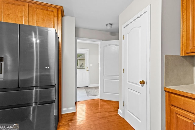 kitchen featuring baseboards, stainless steel fridge with ice dispenser, light wood-style flooring, brown cabinets, and light countertops