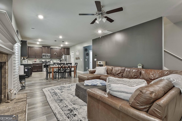 living area with ceiling fan, recessed lighting, a fireplace, baseboards, and light wood-style floors