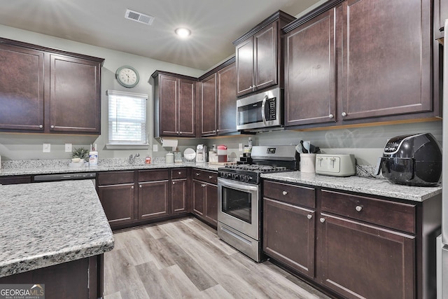 kitchen featuring dark brown cabinetry, light wood finished floors, visible vents, appliances with stainless steel finishes, and a sink