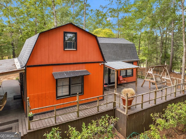 back of house with roof with shingles, a deck, and a gambrel roof