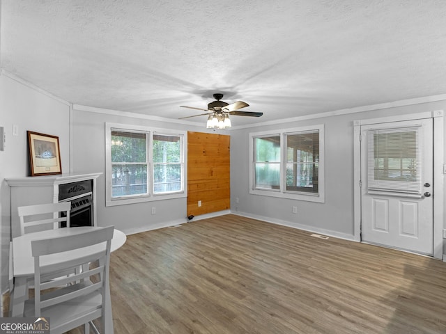 interior space featuring baseboards, a ceiling fan, wood finished floors, crown molding, and a textured ceiling