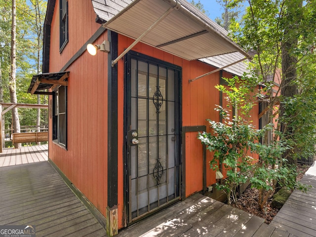 doorway to property with a shingled roof and a deck