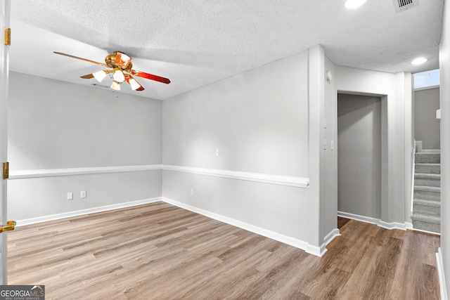 unfurnished room with ceiling fan, a textured ceiling, wood finished floors, baseboards, and stairs