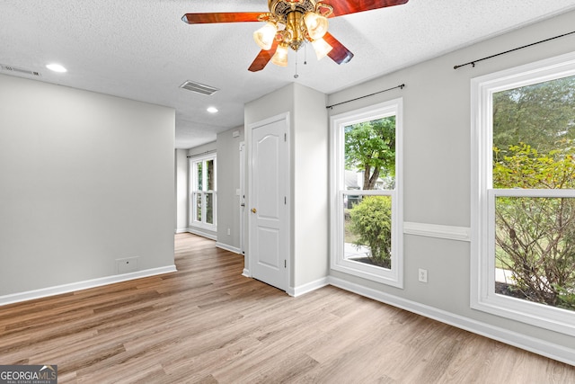 empty room with baseboards, visible vents, a textured ceiling, and light wood finished floors