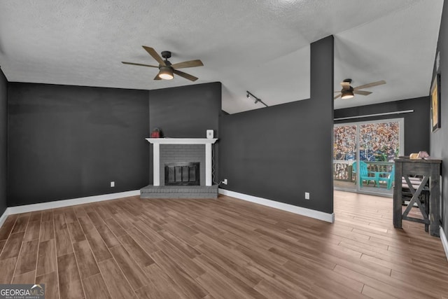 unfurnished living room featuring a textured ceiling, ceiling fan, wood finished floors, baseboards, and a brick fireplace