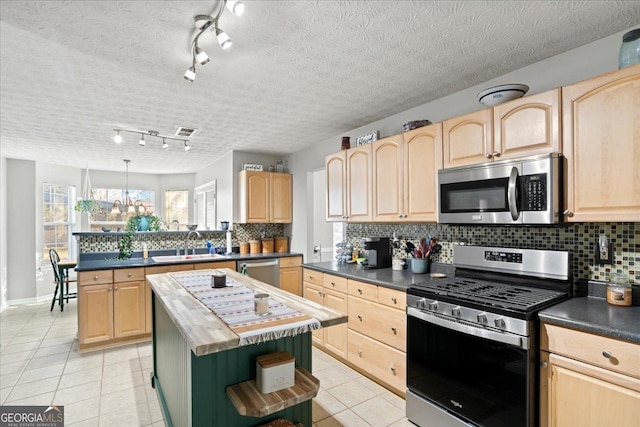 kitchen with light tile patterned floors, dark countertops, appliances with stainless steel finishes, light brown cabinetry, and a sink