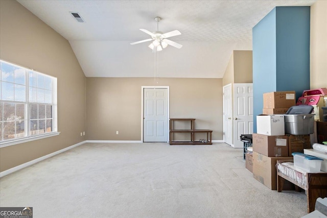 interior space with ceiling fan, light colored carpet, visible vents, baseboards, and vaulted ceiling