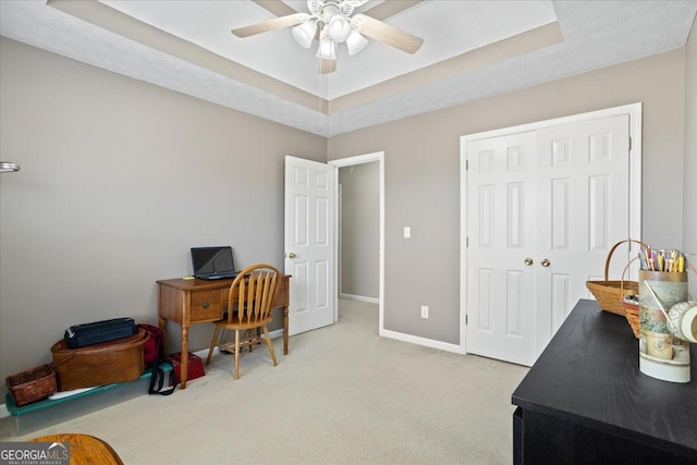 office area with ceiling fan, a tray ceiling, carpet, and baseboards