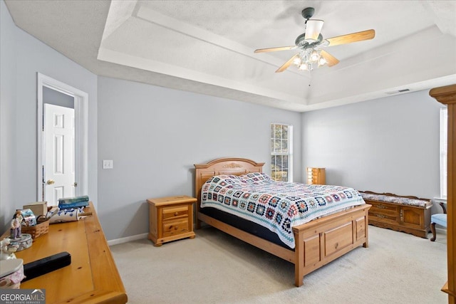 bedroom with visible vents, baseboards, light colored carpet, ceiling fan, and a tray ceiling