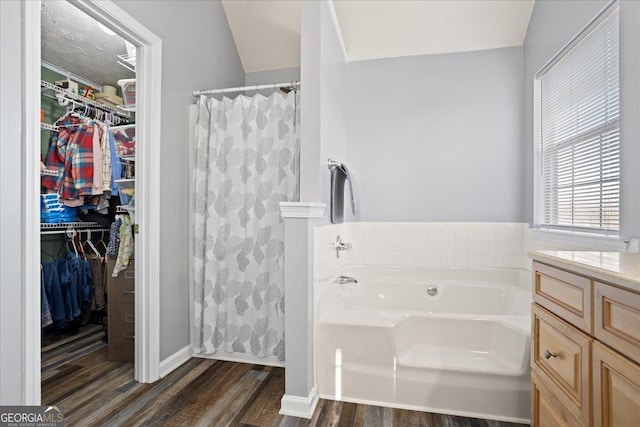 bathroom featuring a garden tub, curtained shower, a spacious closet, vanity, and wood finished floors