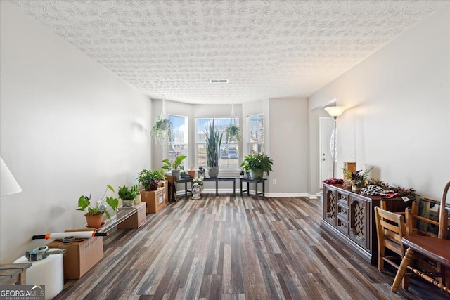 living area featuring baseboards, a textured ceiling, visible vents, and wood finished floors