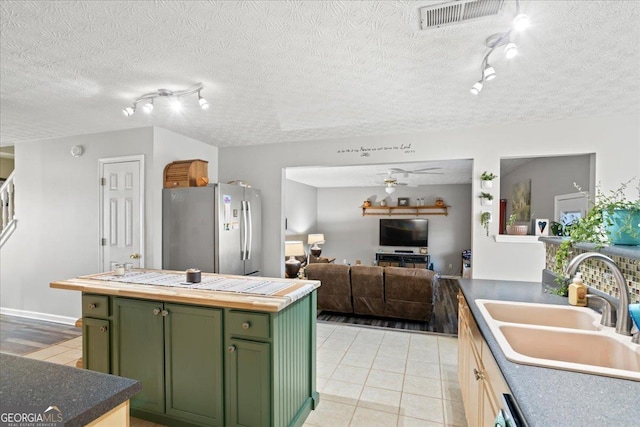 kitchen featuring butcher block counters, visible vents, freestanding refrigerator, a sink, and green cabinetry