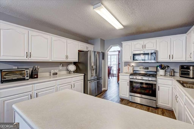 kitchen with a toaster, arched walkways, dark wood-type flooring, stainless steel appliances, and white cabinetry