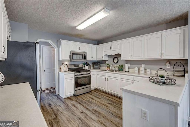 kitchen featuring light wood-style flooring, stainless steel appliances, a sink, white cabinetry, and light countertops