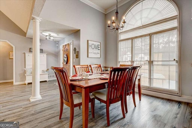 dining space featuring light wood-style floors, decorative columns, ornamental molding, and baseboards