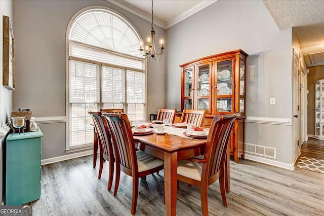 dining space with visible vents, light wood-style flooring, ornamental molding, a chandelier, and baseboards