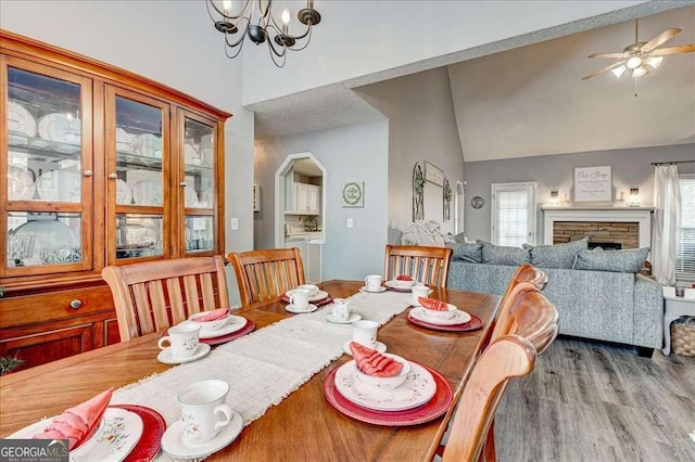 dining space with arched walkways, washer and clothes dryer, vaulted ceiling, a stone fireplace, and wood finished floors