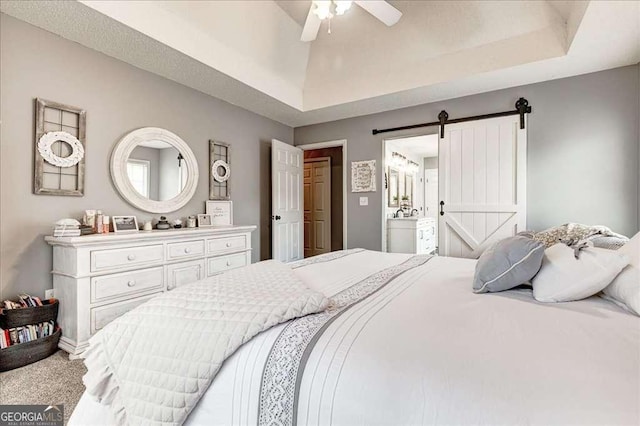 carpeted bedroom featuring ensuite bathroom, a barn door, a raised ceiling, and a ceiling fan