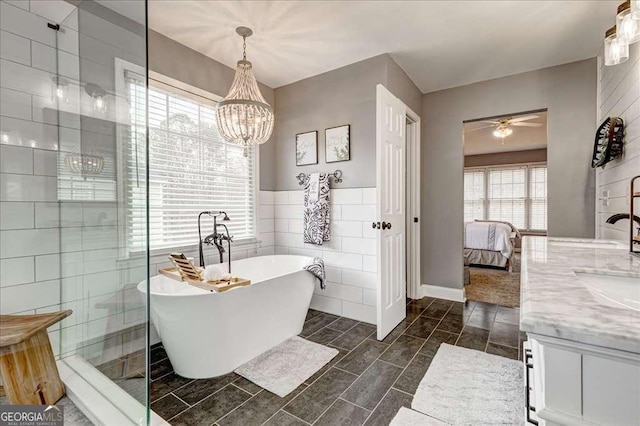 bathroom with tile walls, a freestanding bath, ensuite bathroom, vanity, and ceiling fan with notable chandelier