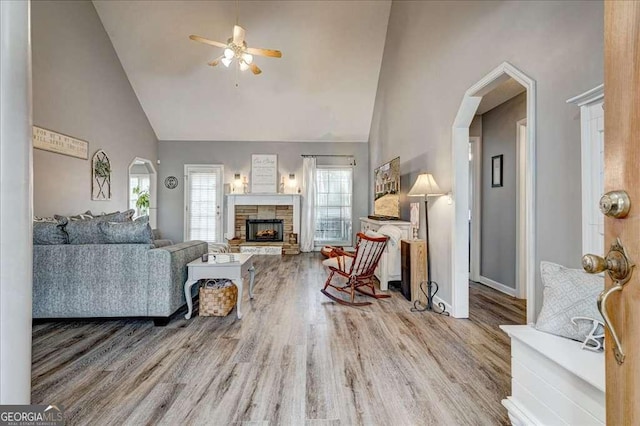 living room featuring high vaulted ceiling, a stone fireplace, and wood finished floors