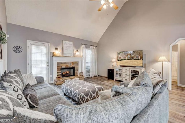 living area with high vaulted ceiling, a stone fireplace, wood finished floors, and a wealth of natural light