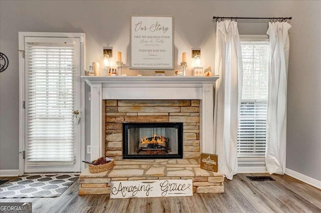 living area with a warm lit fireplace, visible vents, baseboards, and wood finished floors