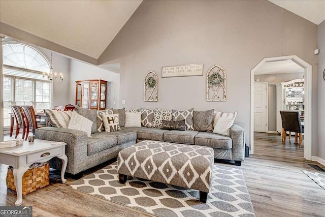 living room featuring arched walkways, high vaulted ceiling, light wood-style flooring, and a notable chandelier