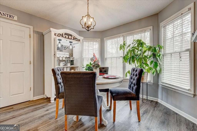 dining area with a textured ceiling, an inviting chandelier, baseboards, and light wood-style floors