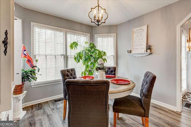 dining space with baseboards, plenty of natural light, an inviting chandelier, and wood finished floors