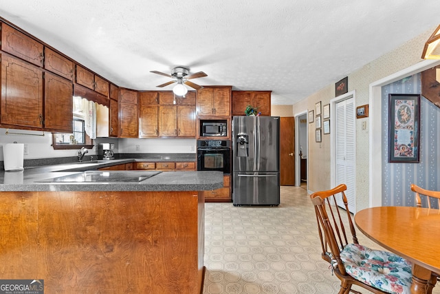 kitchen with brown cabinetry, a textured ceiling, a peninsula, black appliances, and wallpapered walls