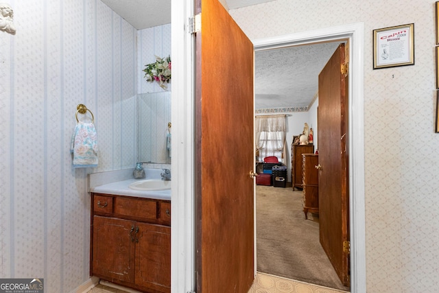 bathroom with a textured ceiling, vanity, and wallpapered walls