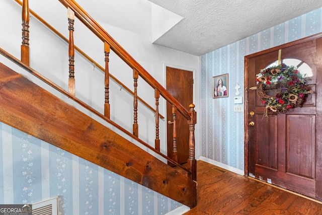 entryway with a textured ceiling, wood finished floors, baseboards, stairs, and wallpapered walls