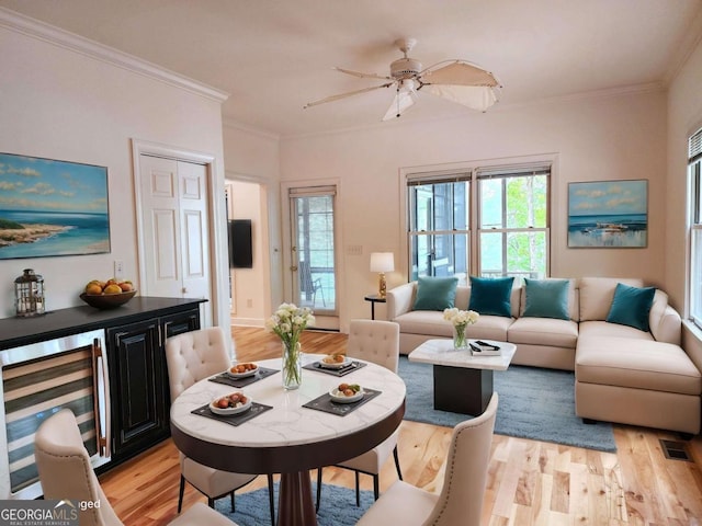 living room featuring crown molding, visible vents, light wood-style flooring, a healthy amount of sunlight, and beverage cooler