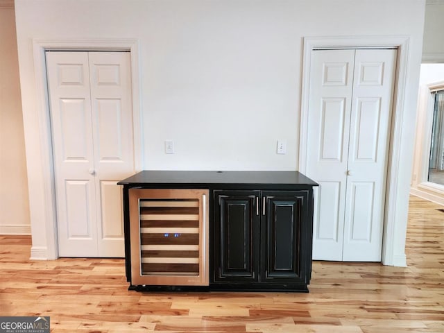 bar featuring beverage cooler, a bar, and light wood finished floors