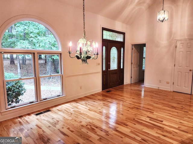 foyer entrance with an inviting chandelier, visible vents, light wood-style floors, and high vaulted ceiling