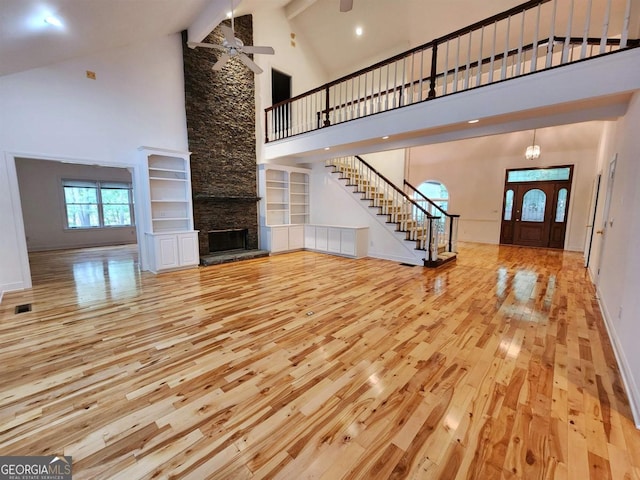 unfurnished living room featuring stairs, a stone fireplace, high vaulted ceiling, baseboards, and hardwood / wood-style flooring