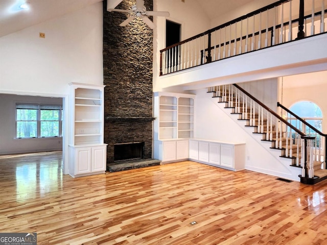 unfurnished living room featuring ceiling fan, high vaulted ceiling, a fireplace, wood finished floors, and stairs