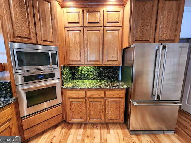 kitchen with stainless steel appliances, light wood finished floors, decorative backsplash, and brown cabinets