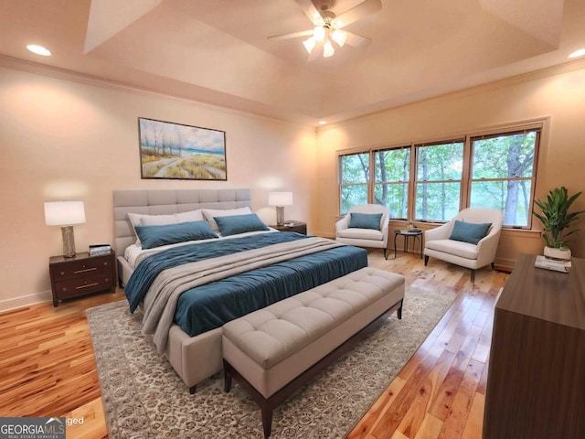 bedroom with crown molding, a tray ceiling, baseboards, and light wood-style floors