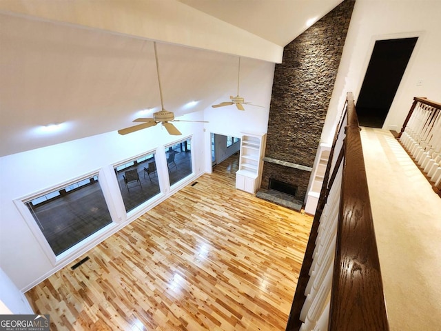 unfurnished living room with high vaulted ceiling, visible vents, a stone fireplace, and wood finished floors