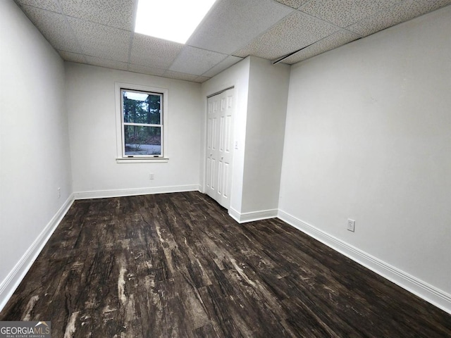 unfurnished bedroom featuring a paneled ceiling, a closet, baseboards, and wood finished floors