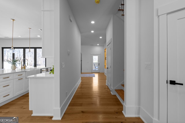 corridor featuring recessed lighting, light wood-style floors, a sink, baseboards, and stairs