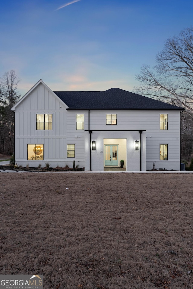 back of property at dusk featuring roof with shingles and board and batten siding