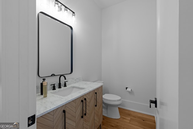 half bathroom featuring vanity, wood finished floors, toilet, and baseboards