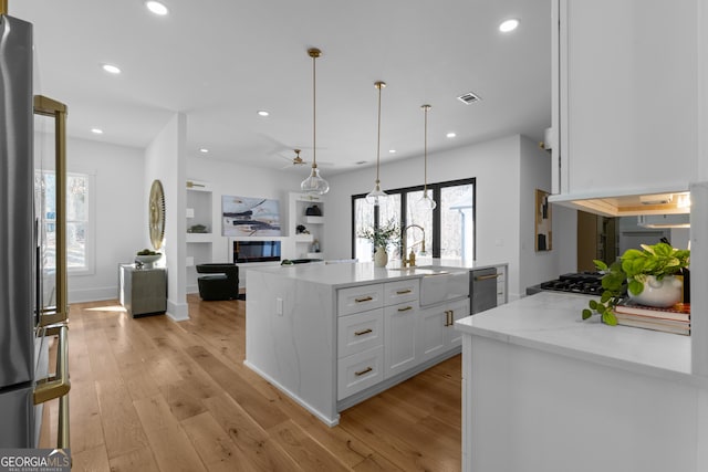 kitchen featuring light wood-style floors, white cabinetry, a sink, and a glass covered fireplace